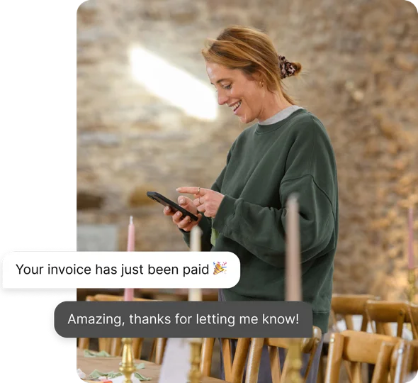 Business owner smiling at their phone as an ANNA notification confirms their invoice has been paid